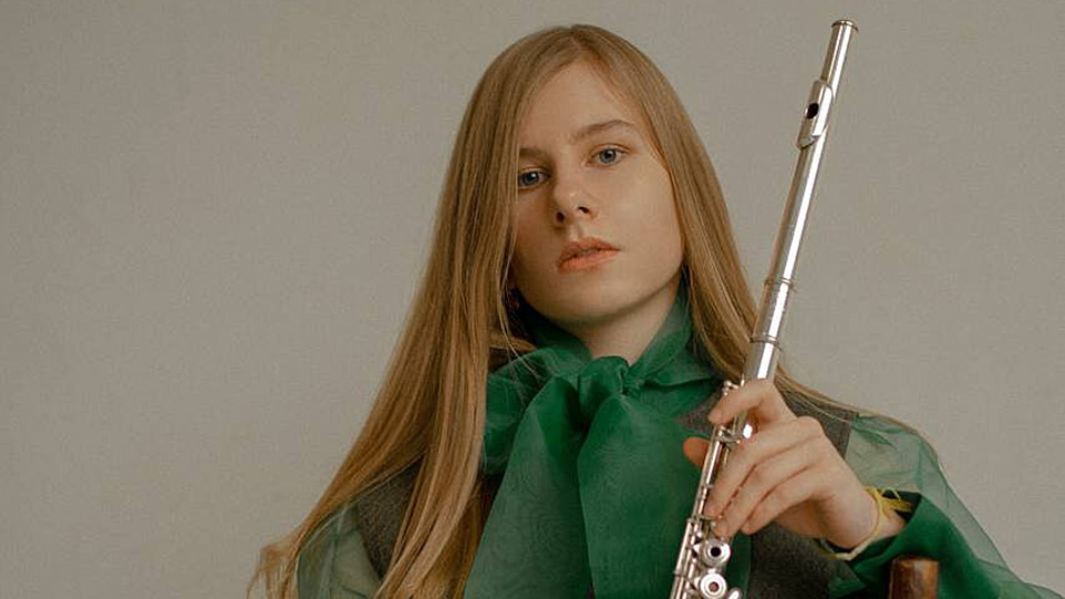 A women, with fair hair, holding a flute, looking at the camera.